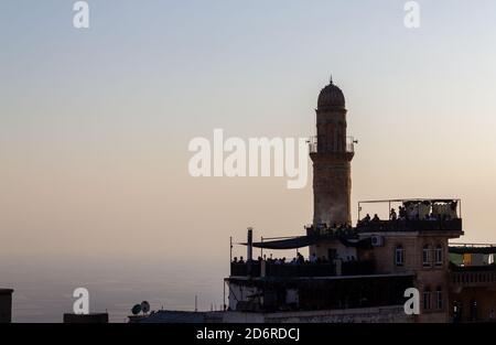 Menschen sitzen in einer Moschee Minarett und Café in der alten Stadt Mardin bei Sonnenuntergang. Skyline von Mardin. Türkei Stockfoto