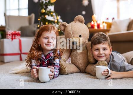 Kleine Mädchen und Jungen in Pyjamas drinnen zu Hause zu Weihnachten, Blick auf die Kamera. Stockfoto