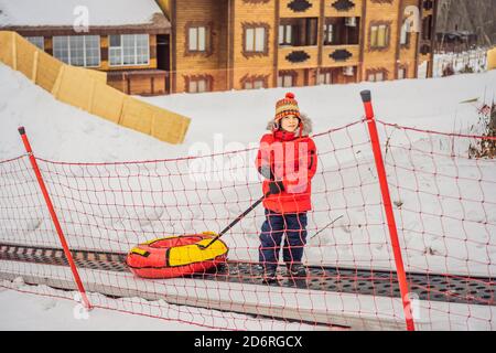 Junge mit Schlauch steigt auf einem Travelator auf den Berg. Kind hat Spaß an der Schneeröhre. Junge reitet einen Schlauch. Winterspaß für Kinder Stockfoto