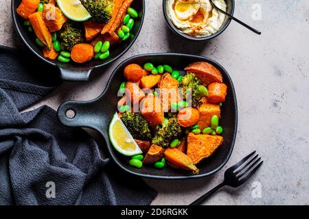 Gebackenes Gemüse in gusseisernen Pfannen, dunkler Hintergrund. Gebackene Süßkartoffeln, Brokkoli, Karotten und Bohnen. Stockfoto