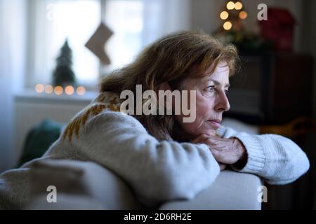 Einsame ältere Frau sitzt auf dem Sofa drinnen zu Weihnachten, Einsamkeit Konzept. Stockfoto