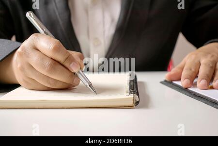 Nahaufnahme einer Geschäftsfrau, die mit einem Stift ein Schreibtischnotizbuch aus Holz und eine Memoliste schreibt. Stockfoto