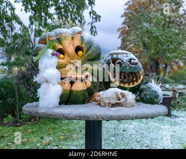 Erster Schnee, geschnitzte dekorative Kürbisse im Garten, ein kleiner Schneemann neben Kürbisdekoren, erster Schnee auf Kürbisdekoren, halloween, Herbstzeit Stockfoto