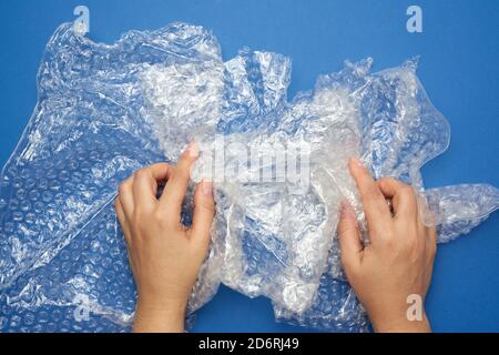 Weibliche Hand hält zerknittertes Stück Polyethylen mit Luftblasen auf einem blauen Holzhintergrund, Verpackungsmaterial Stockfoto