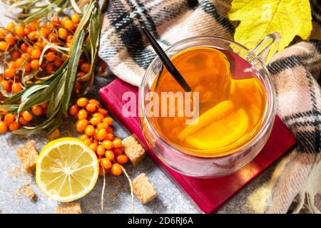 Gesundes Herbstvitamingetränk. Heißer Sanddorntee mit Zitrone mit frischen Sanddornbeeren auf einer steinernen Arbeitsplatte. Stockfoto