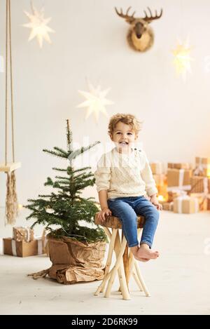 Schöner lockiger kleiner Junge schmückte einen Weihnachtsbaum in einem Weißes Zimmer Stockfoto