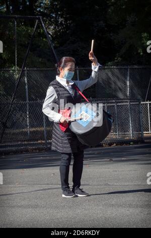 Ein asiatisch-amerikanisches Mitglied eines Trommelensembles probt in einem Park in Queens, New York City, während es eine chirurgische Maske trägt. Stockfoto