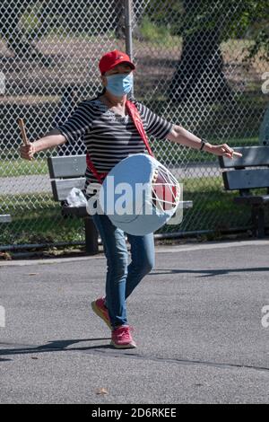 Ein asiatisch-amerikanisches Mitglied eines Trommelensembles probt in einem Park in Queens, New York City, während es eine chirurgische Maske trägt. Stockfoto