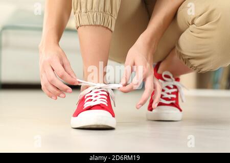 Vorderansicht Nahaufnahme der Frau binden Schnürsenkel von Turnschuhen Auf dem Boden im Wohnzimmer zu Hause Stockfoto