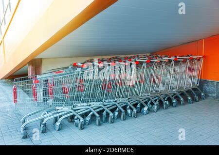 Viele Metall-Einkaufswagen auf einem Parkplatz in der Nähe von Supermarkt im Freien, unter der Treppe stehen Stockfoto