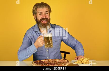 Glücklicher bärtiger Mann mit Bier und Pizza. italienisches Essen. Pommes Frites. Mann in der Bar Bier Glas trinken und Pizza essen. Cheers. Fußball im Fernsehen. american Fast Food. Stockfoto