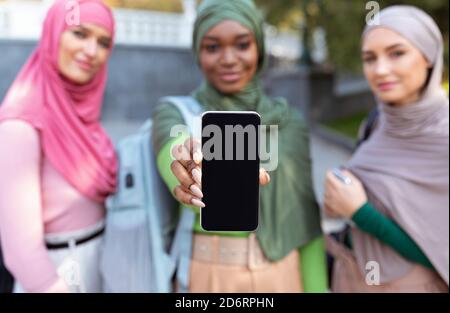 Drei Muslimische Frauen Zeigen Smartphone-Bildschirm Im Freien, Fokus Auf Telefon Stockfoto