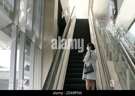Geschäftsfrau mit Gesichtsmaske auf einer Rolltreppe stehend, nach oben Stockfoto