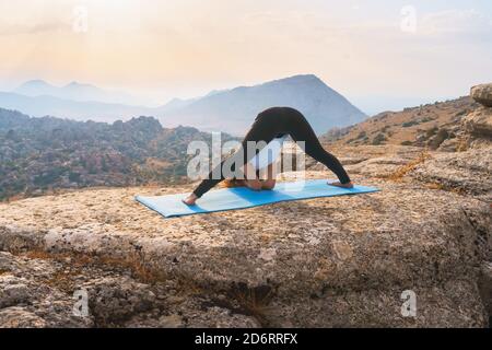 Ganzkörper-Rückansicht der unkenntlich schlanken weiblichen tun Variation Der breiten legged Forward Bend Pose mit Ellbogen auf Matte Beim Yoga auf felsigen m üben Stockfoto