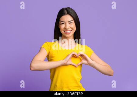 Freundliche asiatische Frau formt Hände wie Herz, macht Liebe Geste nahe der Brust Stockfoto