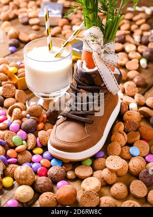 Sinterklaas Holländischer Urlaub. Holzhintergrund mit Kinderschuh mit Karotten für Santa's Pferd, ein Glas Milch, Pepernoten und Süßigkeiten. Hochwertige Fotos Stockfoto