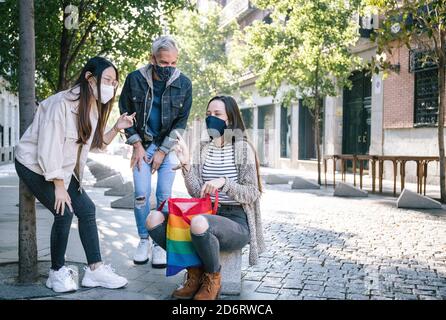 Gruppe von freundlichen verschiedenen Menschen in Schutzmasken versammeln sich auf Straße mit Regenbogen LGBT-Tasche in Madrid und lachend Scherz zusammen Stockfoto