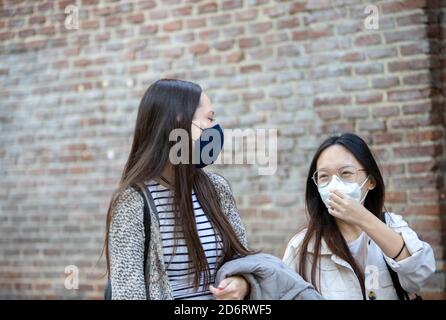 Entzückende multiethnische Freundinnen tragen Schutzmasken zu Fuß in Madrid Und genießen Wochenende zusammen während Coronavirus-Epidemie Stockfoto