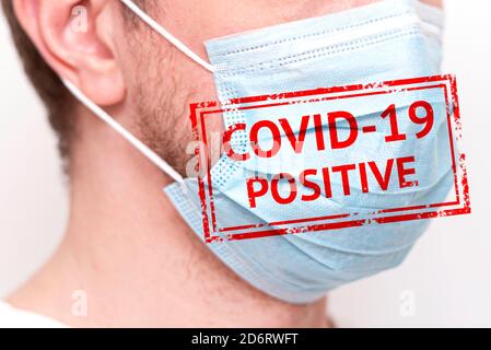Nahaufnahme des Menschen mit Schutzmaske, medizinische Maske auf menschlichem Gesicht mit Text COVID-19 POSITIV, Konzeptbild Stockfoto
