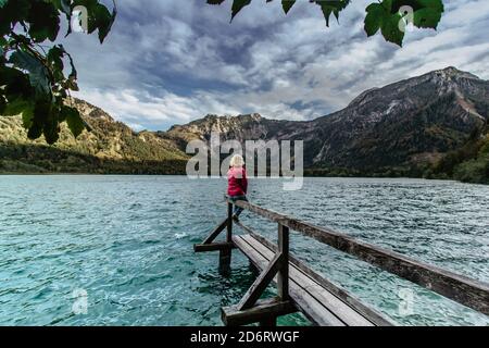 Junges Mädchen mit einer Pause am Bergsee, Österreich. Weibliche Reisende mit Blick auf die Alpen. Reiselust Freiheit Reisekonzept. Sommerurlaub Abenteuer Stockfoto