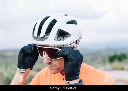 Zuversichtlich männlichen Radfahrer im Helm setzen auf schützende Sonnenbrille, während In der Natur stehen und sich auf das Reiten vorbereiten Stockfoto