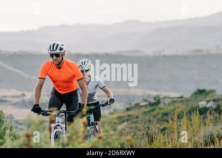 Seriöse professionelle Radfahrer in Helmen und Sonnenbrillen Reiten bergauf in hochland während des Trainings im Sommer Stockfoto