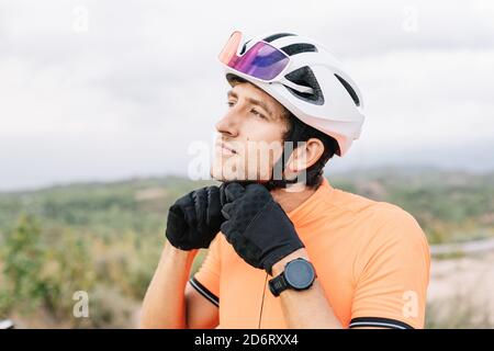 Calm männlichen Radfahrer stehen in der Natur und setzen auf Schutz Helm während der Vorbereitung für Fahrrad fahren und wegschauen Stockfoto