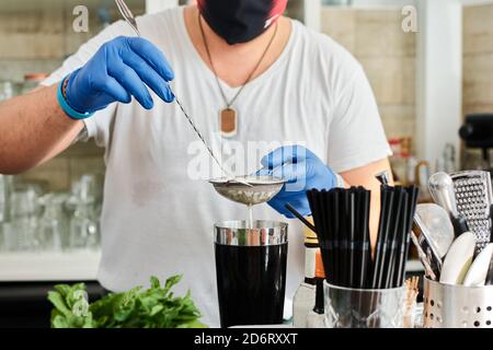 Anonymous Ernte männlichen Barkeeper in Maske und Handschuhe Gießen Milch In den Shaker während der Zubereitung von leckeren Smoothie im Café Stockfoto