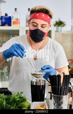 Männlicher Barkeeper in Maske und Handschuhen, der Milch in den Shaker gießt Während der Zubereitung von leckeren Smoothie im Café Stockfoto