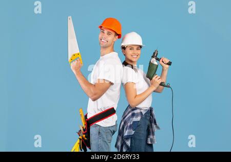 Reparaturteam. Glückliches Paar In Harten Hüten Posiert Mit Säge Und Drill Stockfoto