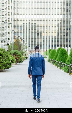 Rückansicht des selbstbewussten erwachsenen afroamerikanischen männlichen Unternehmers in Eleganter blauer Anzug mit Krawatte, die beim Gegenstehen wegschaut Verschwommenes städtisches Backgr Stockfoto