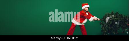 Mädchen in santa claus Kleid ziehen einen Weihnachtsbaum für die Einrichtung. Mädchen gekleidet als Santa Claus, ein Weihnachtsbaum. Stockfoto