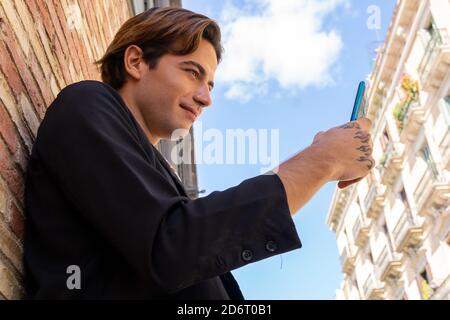 Von unten Seitenansicht des jungen Inhalts stilvolle tätowierte männlich SMS auf Handy unter blauem bewölktem Himmel Stockfoto