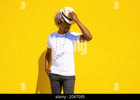 Schwarzer Mann mit Afro-Haaren, der auf einem gelben Hintergrund einen Strohhut aufsetzt. Hat-Konzept. Stockfoto