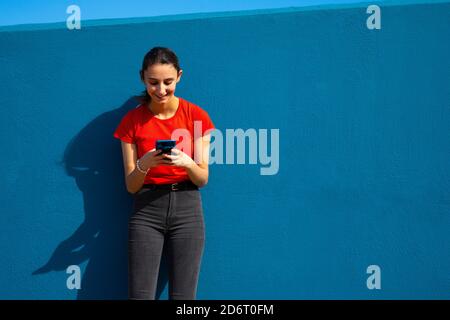 Frau in rot gekleidet mit dem Handy auf blauem Hintergrund. Konzept der Nutzung des Mobils. Blauer Hintergrund. Stockfoto