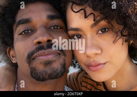 Fröhlicher junger schwarzer Mann und Frau mit Afro-Frisur, die kuscheln und an sonnigen Tagen die Kamera betrachten Stockfoto