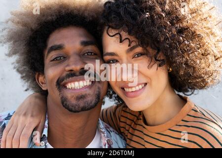 Fröhlicher junger schwarzer Mann und Frau mit Afro-Frisur, die kuscheln und an sonnigen Tagen die Kamera betrachten Stockfoto