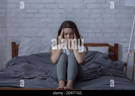 Negative Emotionen und psychische Gesundheit Konzept. Einsame junge Frau fühlt sich deprimiert, sitzt Kopf in den Händen im Schlafzimmer Stockfoto