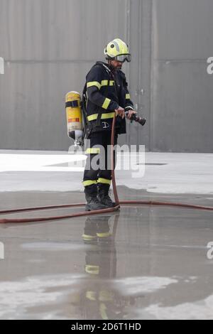 Anonymer Feuerwehrmann in Uniform und Schutzhelm stehend mit Feuer Feuerlöscher und Gummischlauch auf der Fahrbahn während Routinearbeiten Stockfoto