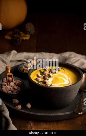 Nahrhafte Kürbissuppe in Schüssel serviert auf Tablett mit knusprig Brotkrusten und Nüsse auf Holztisch Stockfoto