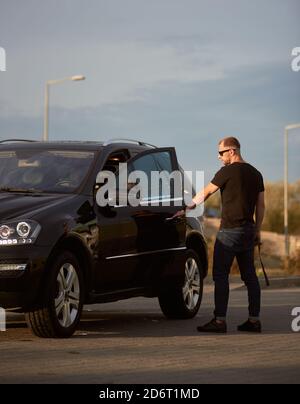 Gut aussehende sportliche Geschäftsmann lässig gekleidet öffnet die Tür seines coolen Autos auf der Straße, Seitenansicht, voller Länge, Kopierer Raum Stockfoto