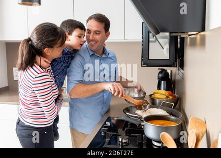 Fröhliche Familie, die neben dem Herd steht und Reis zum Mittagessen kocht Während sie sich mit einem Lächeln anschauend Stockfoto