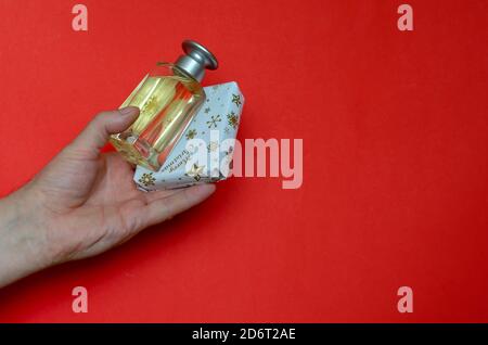 Weihnachtsgeschenk und Flasche Parfüm in der Hand auf rotem Hintergrund. Man's Hand hält verpackte Geschenkbox und Parfüm. Winterurlaub Konzept. Stockfoto