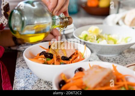 Crop unkenntlich weibliche Gießen Olivenöl in Schalen mit geschnitten Gemüse und Speck in der hellen Küche Stockfoto