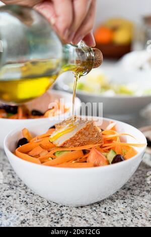 Crop unkenntlich weibliche Gießen Olivenöl in Schalen mit geschnitten Gemüse und Speck in der hellen Küche Stockfoto