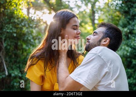 Seitenansicht des jungen bärtigen ethnischen Kerl in der Liebe zu Glückliche Freundin beim gemeinsamen Entspannen im grünen Garten auf sonnig Tag Stockfoto
