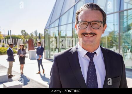 Glücklicher Mann mittleren Alters Manager mit Schnurrbart in edlem Outfit Blick auf die Kamera auf der Straße Stockfoto