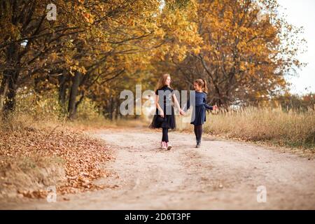 Zwei Mädchen im Teenageralter gehen im warmen Herbst an einer Waldstraße entlang. Stockfoto