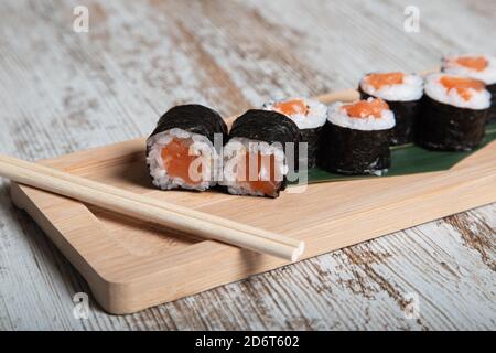 Set japanischer Hosomaki Sushi-Rollen mit frischem Lachsfilet Serviert auf Holzbrett mit Essstäbchen Stockfoto