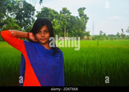 Nahaufnahme eines Teenagers, das Salwar Kameez und blaue dhupatta mit der rechten Hand am Hals trägt, auf einem Reisfeld stehend, selektiv fokussiert Stockfoto